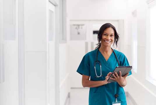 Portrait Of Smiling Female Doctor Wearing Scrubs In Hospital Corridor Holding Digital Tablet healthcare linen nurse.