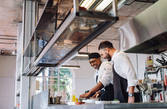 Two cooks preparing food in restaurant kitchen.